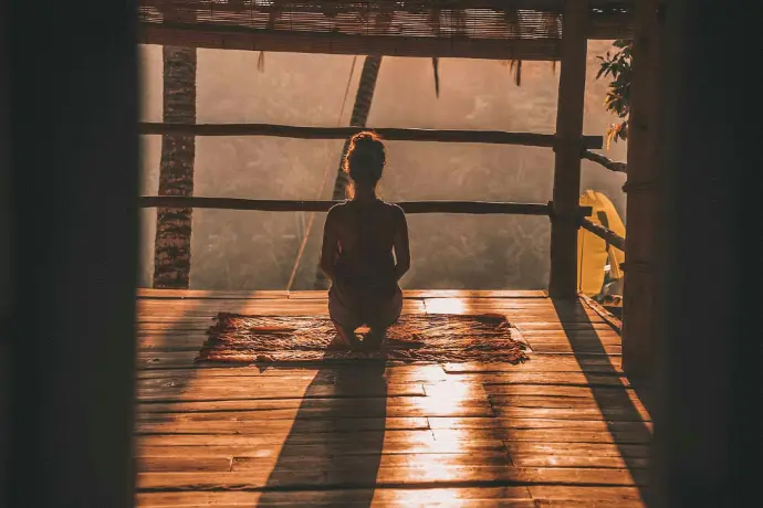 woman meditating on floor with overlooking view of trees